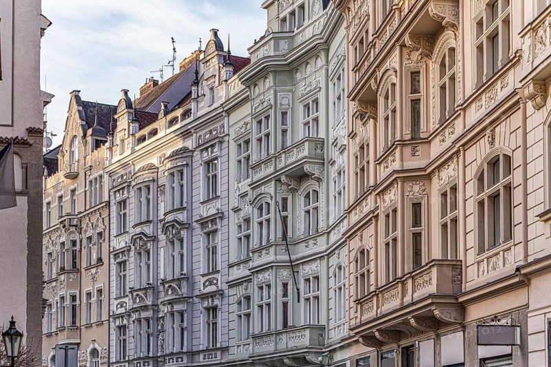 Elegant European facades with ornate architectural details bathed in soft sunlight. The buildings display a harmony of classic design, showcasing urban charm and history of Prague