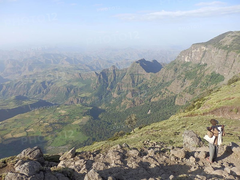 Man with rifle, Kalashnikov, looking at a vast mountain panorama, valleys stretching in the background, Simien National Park, Ethiopia