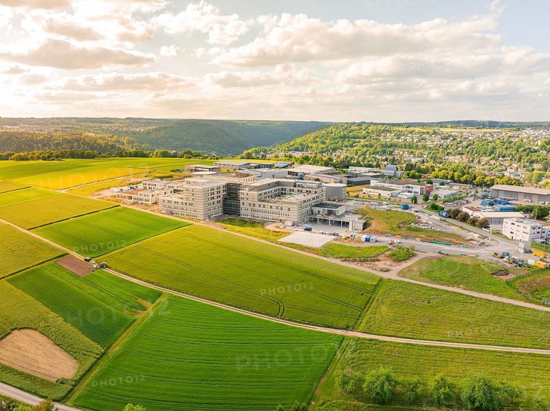 Large building surrounded by extensive green fields, embedded in a hilly landscape, construction of the new hospital health campus Calw, Germany