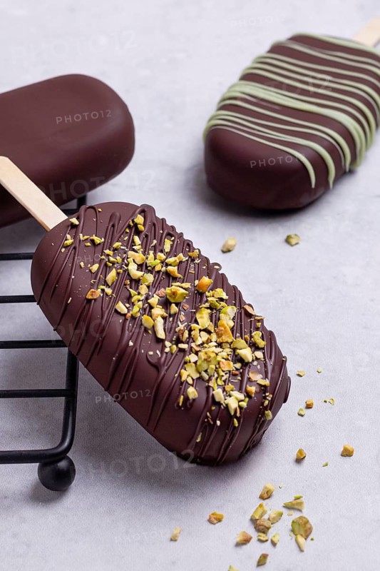 Gourmet chocolate covered ice creams garnished with matcha blend, presented elegantly on a white marble plate, adorned with chopped crushed pistachios, served on a marble surface