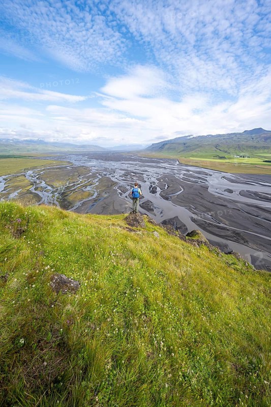 Hiker, young man on a hill, view over alluvial land, meandering river, Dímonarhellir, Suðurland, Iceland