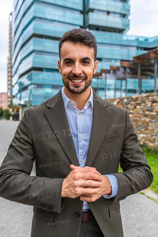 Vertical frontal portrait of a caucasian young businessman wearing suit standing smiling at camera in the city