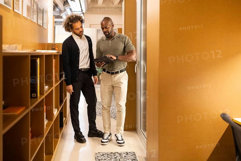 Two professionals engage in a discussion in a stylish coworking space in Barcelona, surrounded by shelves and modern furniture, promoting collaboration and creativity