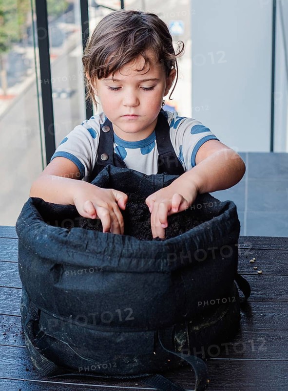 Close-up of a young girl focusing intently as he plants a seed in a fabric grow bag, embodying early learning and nature interaction