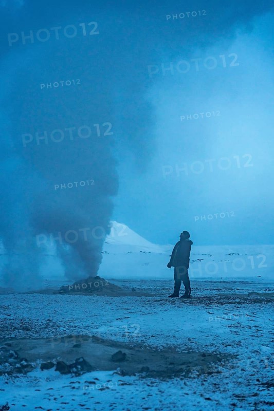 A man stands next to one of the steaming fumaroles at Hverir or Namafjall geothermal park in winter, Iceland