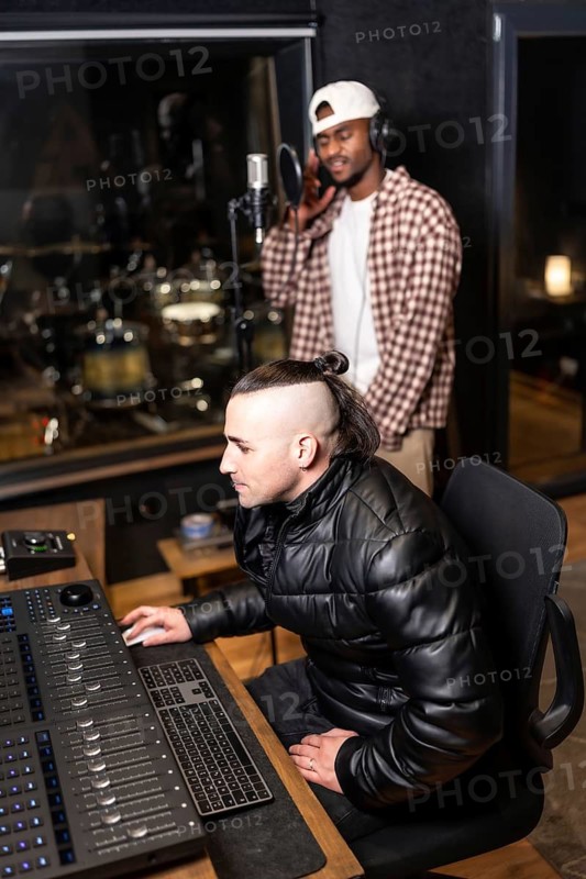 Sound engineer mixing a song while the singer is recording using a professional microphone in a recording studio