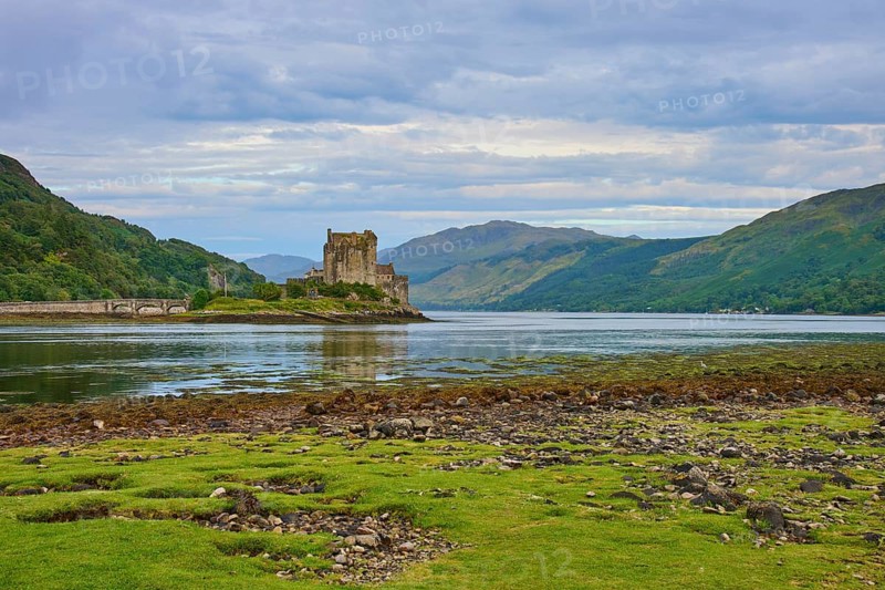 View of a historic riverside castle with mountainous backdrop and cloudy sky, Eilean Donan Castle, Dornie, Kyle of Lochalsh, Scotland, United Kingdom, Great Britain