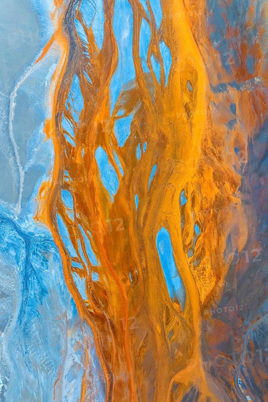 This stunning aerial photograph captures a multicoloured landscape, showcasing an intricate mix of blue and golden hues that resemble fluid art