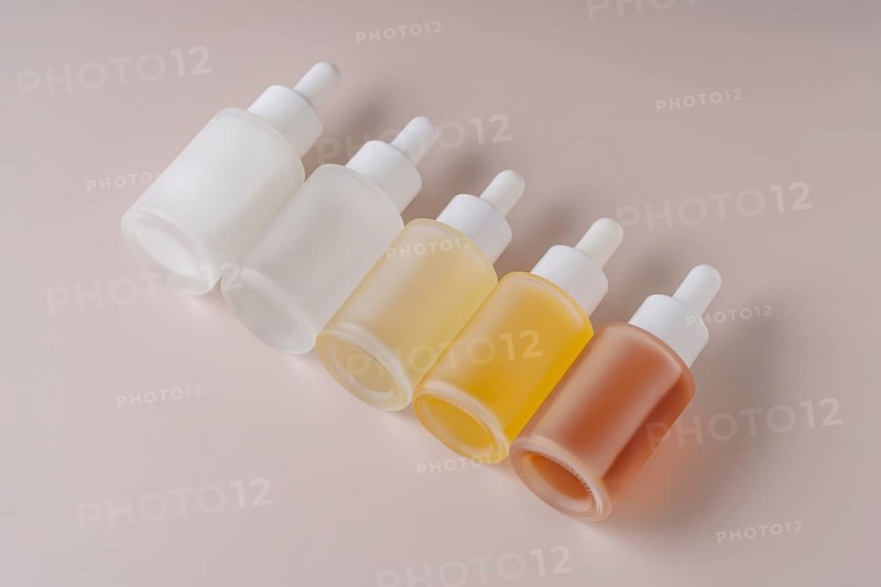 A neatly organized gradient set of five dropper bottles with varying contents from clear to amber displayed against a soft beige background