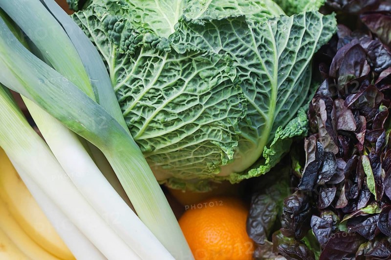 A vibrant mix of fresh produce featuring a variety of colorful fruits and vegetables. This assortment includes crisp greens, leafy cabbage, and a bright orange, showcasing natural beauty