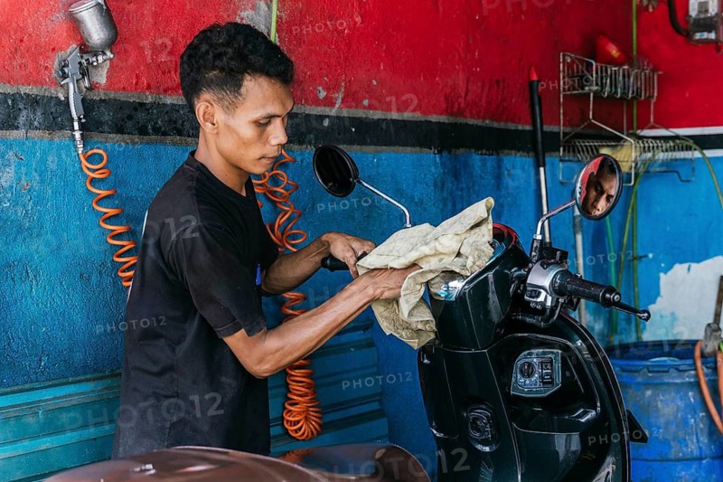 A dedicated worker meticulously cleans a motorcycle at a vibrant garage. The image captures the essence of motorcycle maintenance, featuring tools, a rag, and a spray gun