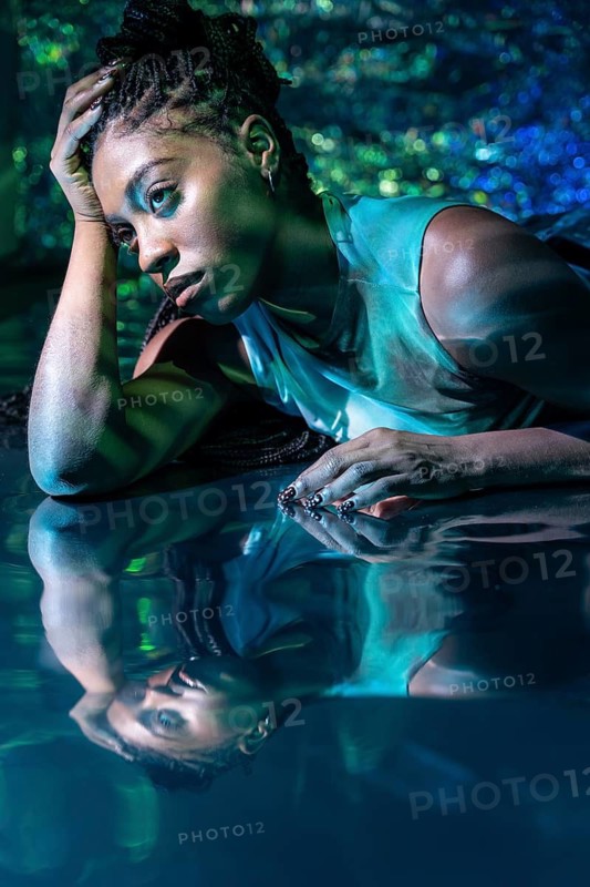 A futuristic African young woman reclines in a digital metaverse landscape, surrounded by glowing colors. Her expression is thoughtful, embodying innovation and virtual reality