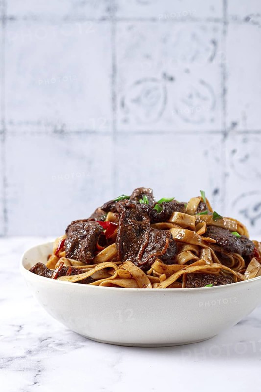 Udon noodles with Mongolian beef, green onions and vegetables, in a white plate, on a light background, homemade, no people