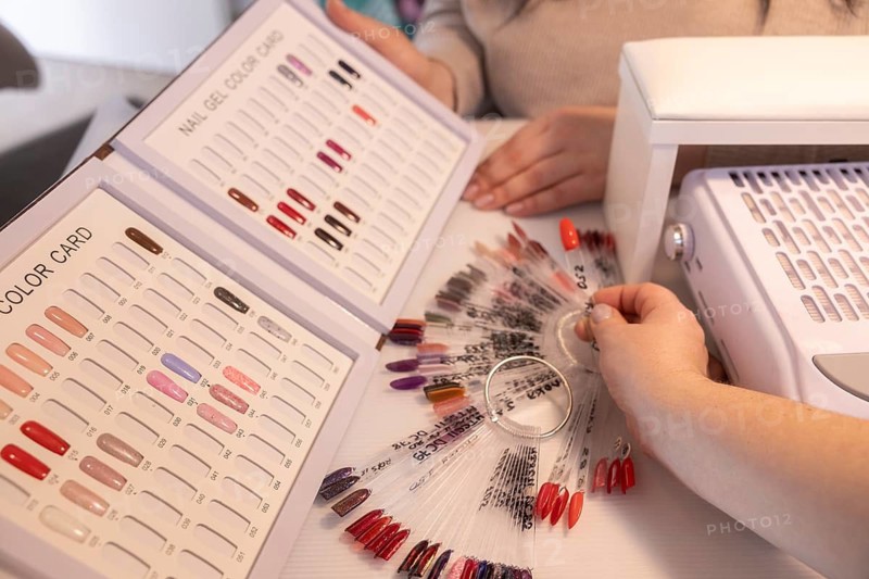 A cozy salon setting with a client choosing nail colors from color cards. The scene captures the essence of beauty treatments