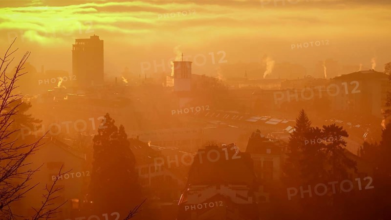 A serene sunrise casts a golden hue over the cityscape of Lausanne, Switzerland, highlighting the silhouettes of buildings against a softly illuminated sky