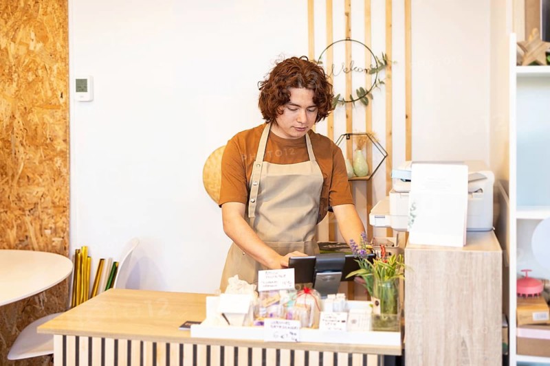 A organic products skin care shop cashier wearing a brown apron works diligently at the counter, surrounded by plants and shop decor, creating a welcoming atmosphere in a store