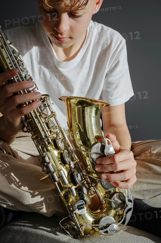 A young musician concentrates while holding a saxophone, captured in natural light. The focus on expression and instrument highlights the passion for music and practice