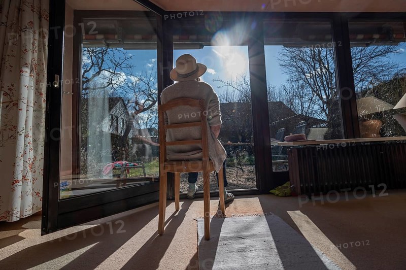 Woman wearing hat sunbathing with patio door open, Bavaria, Germany
