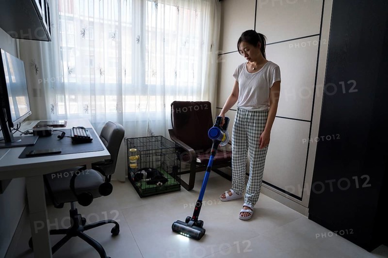A woman efficiently cleans her living room using a sleek modern vacuum cleaner. The setting is bright and organized with natural light streaming through large windows