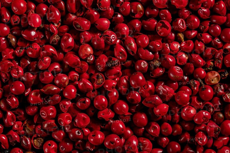 Densely packed red peppercorns with a vibrant color and some with visible stems, showing varied shades and textures