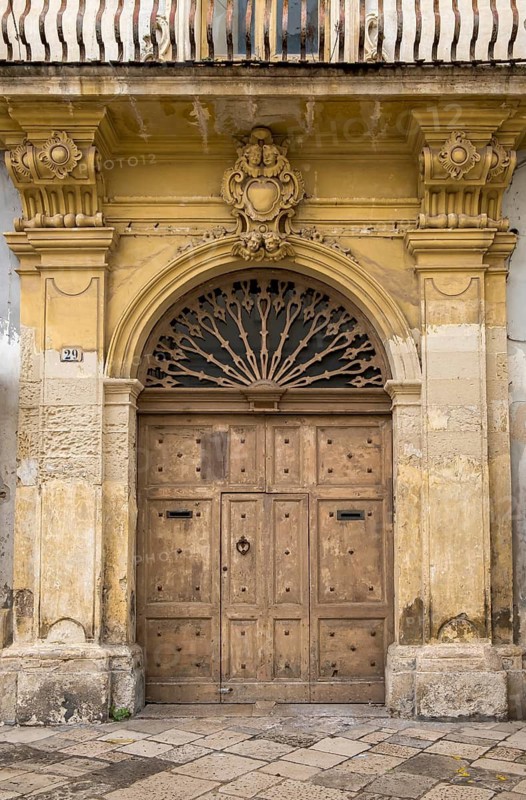 Old decorated stone portal with weathered wooden door and yellowish facets, old town centre of Galatina, Apulia, Italy