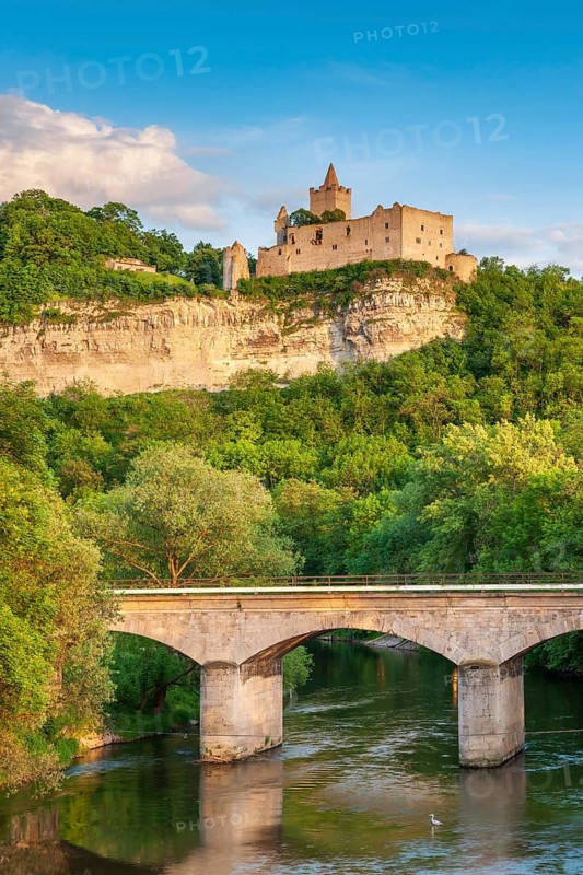 View of the Rudelsburg castle ruins above the Saale river with railway bridge in the evening light, a grey heron in the water, Saale valley, near Bad Kösen, Saxony-Anhalt, Germany