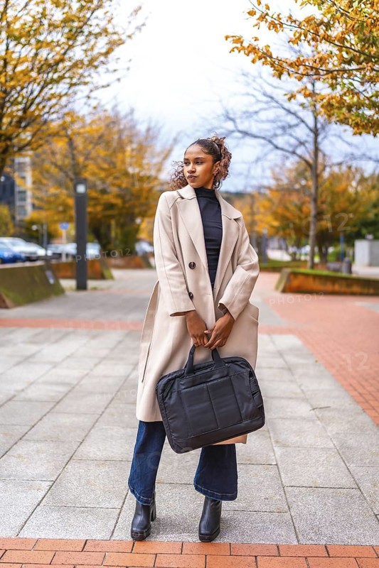 Vertical full length photo of a business style african american model with trench coat and handbag posing outdoors