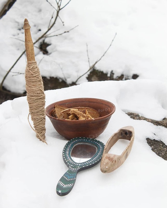 Spindle, mirror and clay plate with bread in the snow. Pagan altar, offering of gifts. Still life