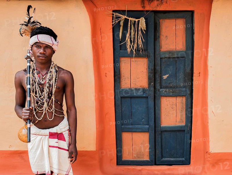 Portrait of a traditionally dressed teenage boy from the Dhurwa tribe (Odisha, India), door of a tribal house