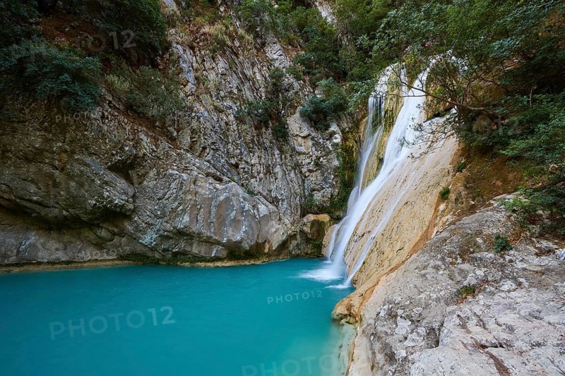 A waterfall flows over rocks into a tranquil turquoise pool surrounded by thick vegetation, waterfalls, ponds, Polylimnio, Peloponnese, Greece