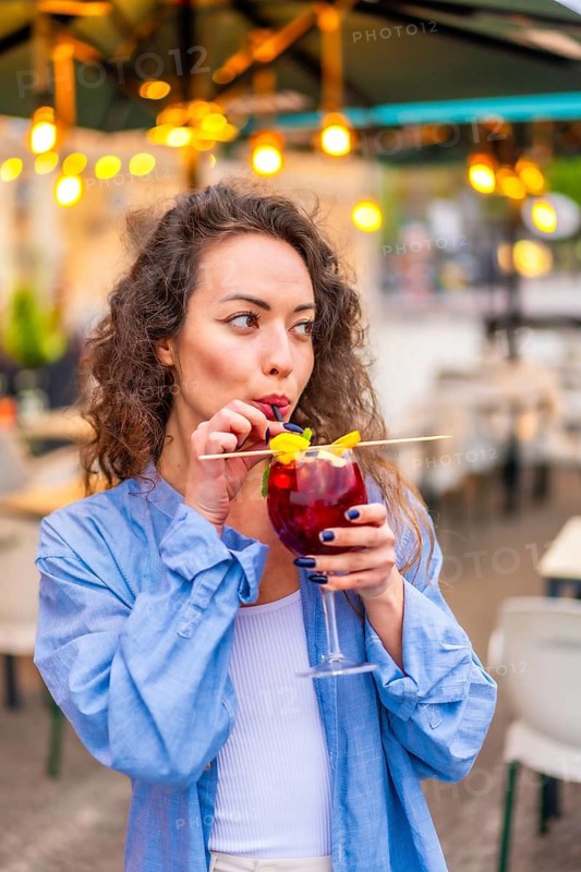 Vertical portrait of a beauty adult caucasian woman using straw drinking cocktail in a terrace