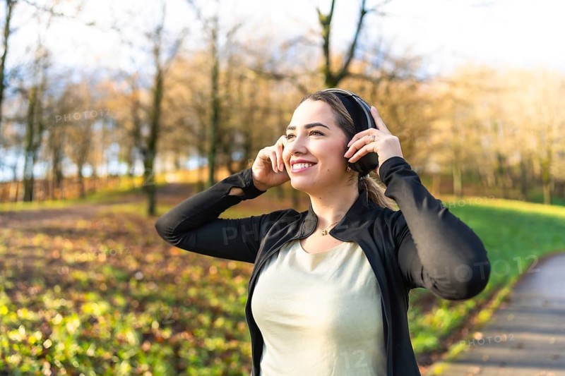 Happy young woman smiling and enjoying listening to music through headphones, finding emotional connection and joy while walking outdoors in an autumn park