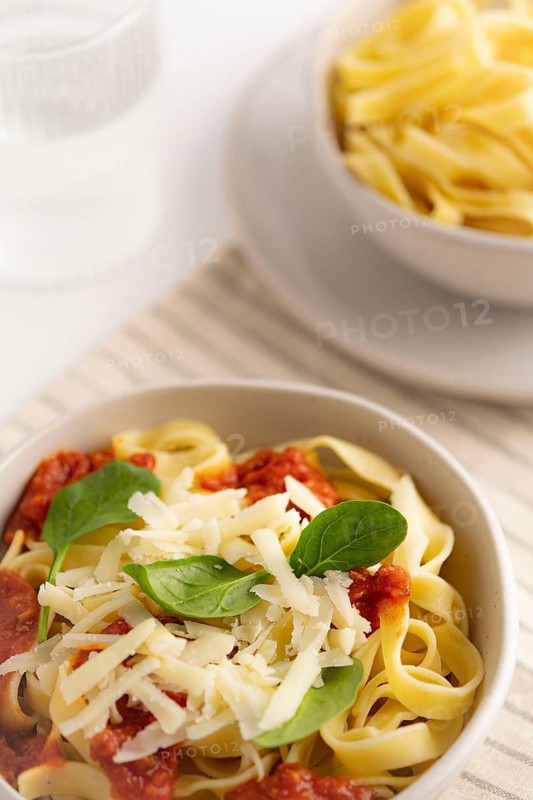 A close up of spaghetti topped with vibrant tomato sauce, grated cheese, and fresh spinach in a bowl. Background features a bowl of plain pasta. Ideal for culinary content