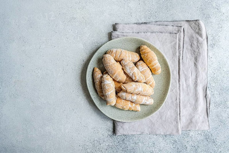 From above, a plate of homemade croissants dusted with flour sits on a textured surface. The pastries are arranged neatly, showcasing their flaky, golden-brown layers