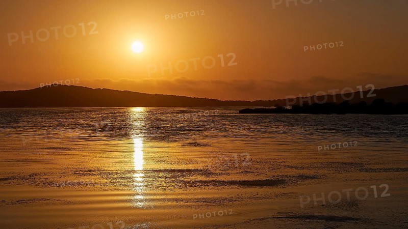 Sunset over calm sea with golden hues and distant hills, Gialova lagoon, protected wetland, bird paradise, Navarino Bay, Pylos, Peloponnese, Greece