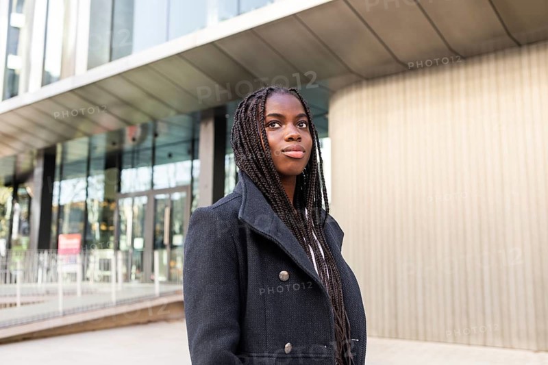 A young professional African American businesswoman with long braids outdoors, looking away confident in a business setting