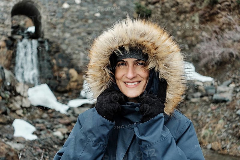 Smiling woman in a fur-lined hooded coat at Astun ski resort, Huesca Pyrenees. Snow and stone bridge in the background create a serene winter atmosphere