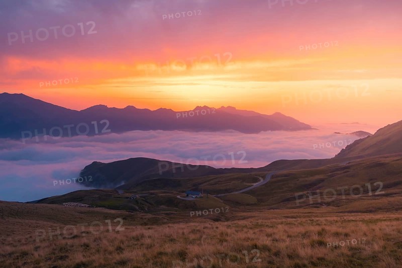 Experience serenity with a mountainous landscape bathed in vibrant sunset hues in the Pyrenees. Soft clouds drift below the peaks, creating a harmonious scene of nature is beauty in summer