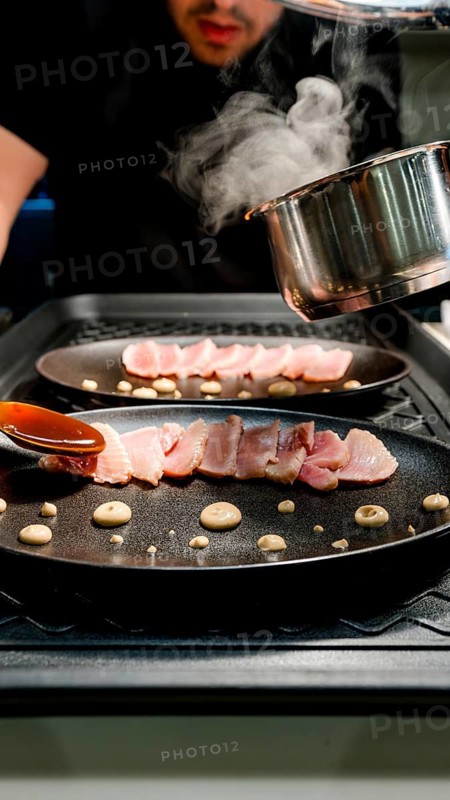 A chef skillfully sears fresh tuna slices, arranging them elegantly on a pan with rich sauces and garnishes, showcasing fine dining culinary artistry in a restaurant setting