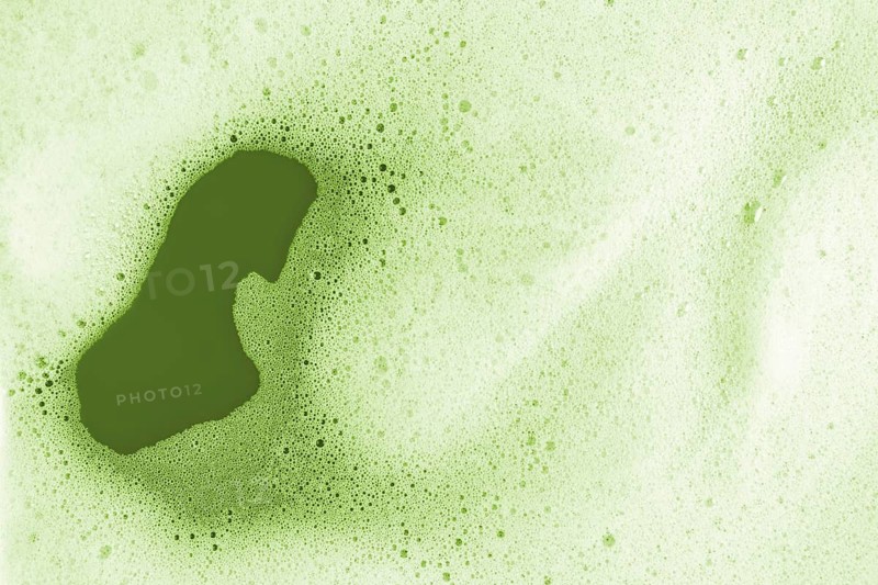 A detailed macro photograph showcasing the vibrant green texture of matcha foam. Tiny bubbles and rich color create an intriguing abstract pattern on the surface