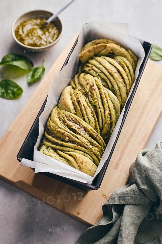 Baked homemade savoury babka plaited bread loaf flavoured with cheese and pesto, in the making tin