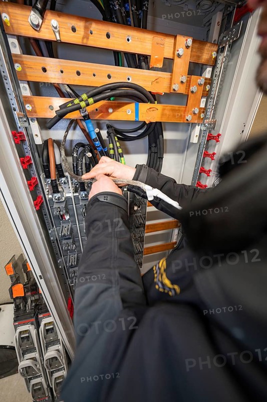 Worker working on cables in an open power box, focus on installation and technology, switch cabinet construction, PV system construction, major customers, Enzkreis, Germany