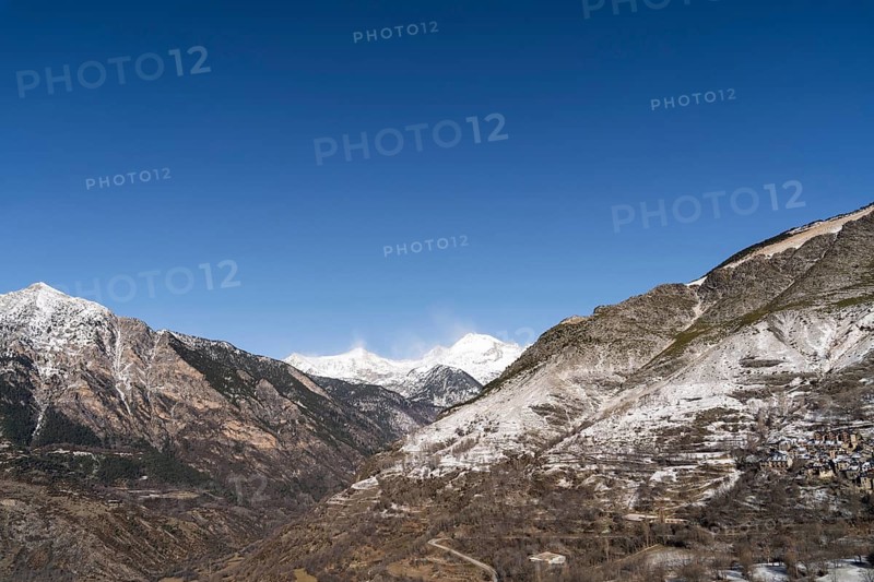 A breathtaking rural landscape featuring majestic snow-capped mountains under a clear blue sky, with a small village nestled on the slopes