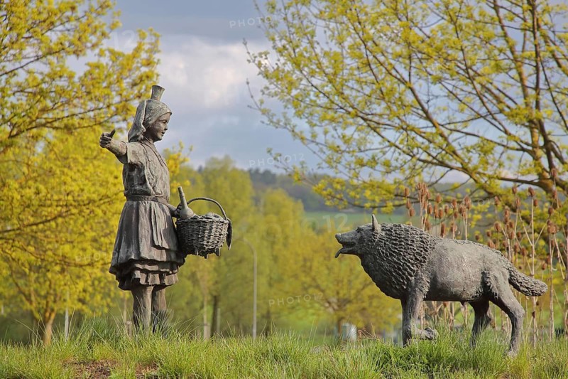 Little Red Riding Hood sculpture by Ewald Rumpf 2010, modern art, bronze sculpture, girl with wicker basket and traditional costume, fairytale figure and the bad wolf, wolf figure, gesture, arm stretching, German Fairytale Route, Remsfeld, Knüllwald, Knüllgebirge, Hesse, Germany