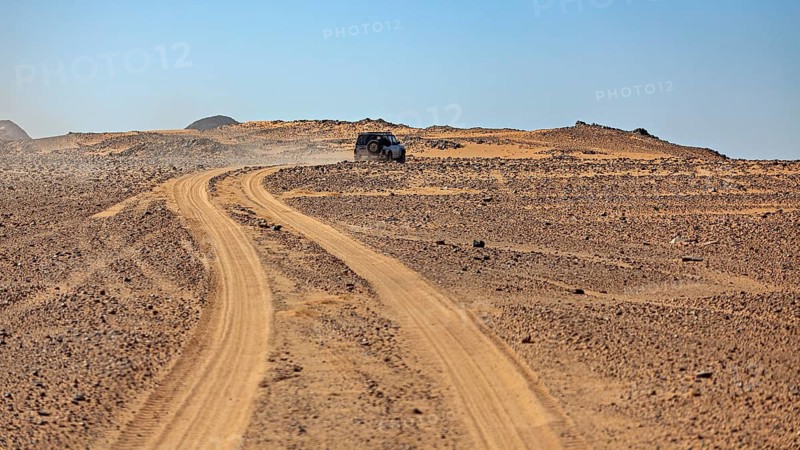 An off-road vehicle on a dusty road in a vast, barren desert landscape, off-road by car through the landscapes of the Sahara in Algeria
