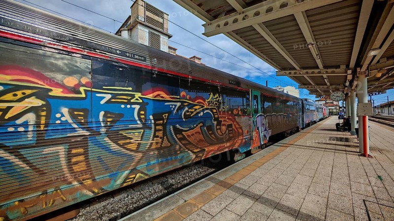 A colorful train decorated with graffiti stands at the train station, surrounded by summer sky, Faro, Algarve, Portugal