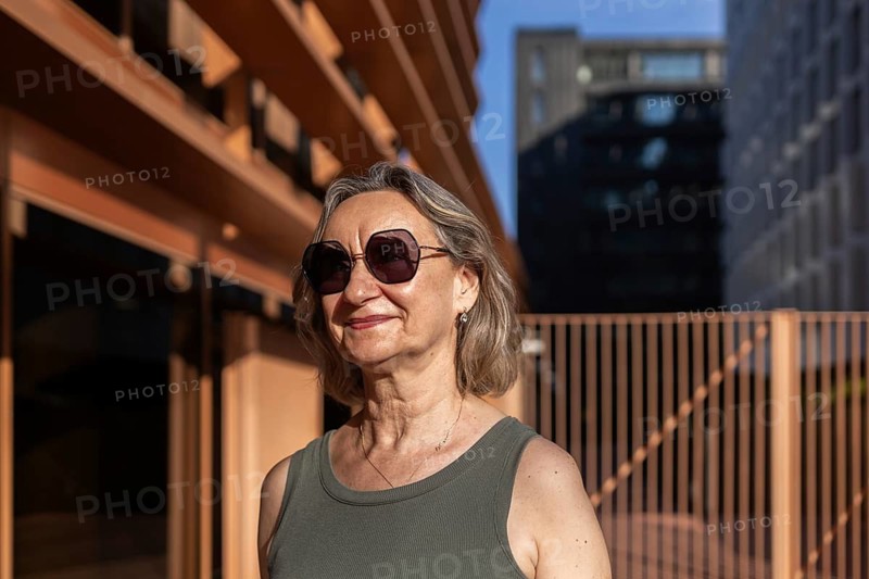 A confident woman wearing sunglasses and a tank top enjoys the sunshine in the city. She exudes a relaxed and content vibe, embracing her vibrant lifestyle