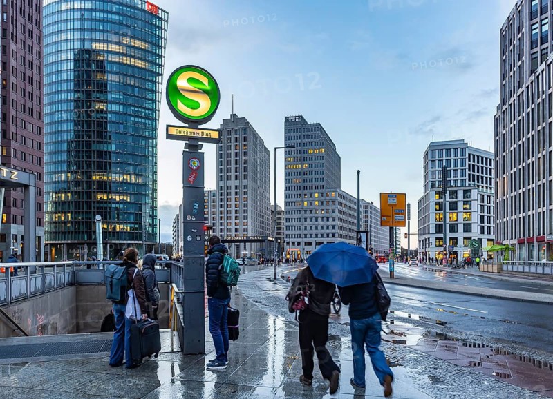 Potsdamer Platz Berlin in the evening with traffic on the streets. When it rains, the skyscrapers are reflected in puddles of water. People traveling with umbrellas. Berlin, Germany
