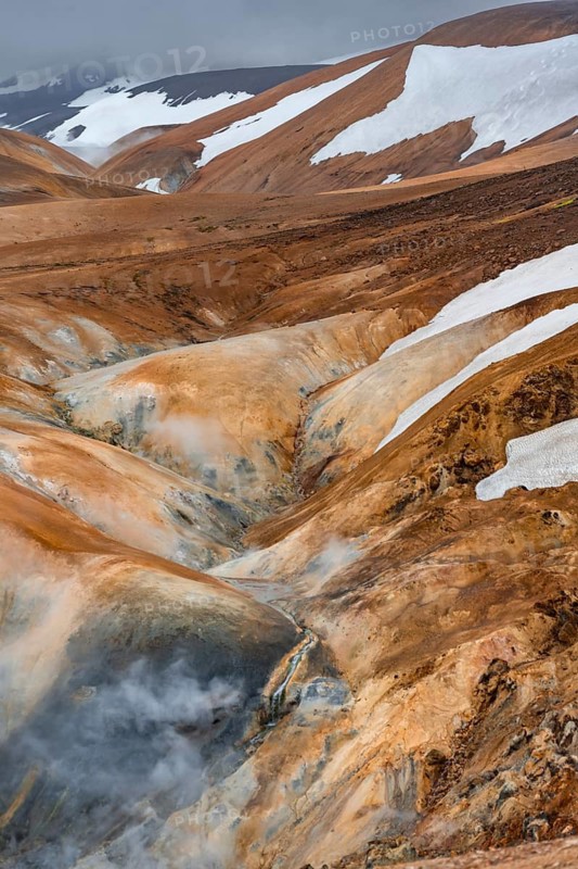Steaming stream between colourful rhyolite mountains with snowfields, Hveradalir geothermal area, Kerlingarfjöll, Icelandic highlands, Iceland