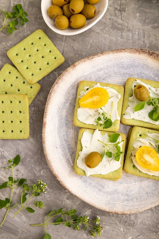 Green cracker sandwiches with cream cheese and cherry tomatoes on gray concrete background. top view, flat lay, close up